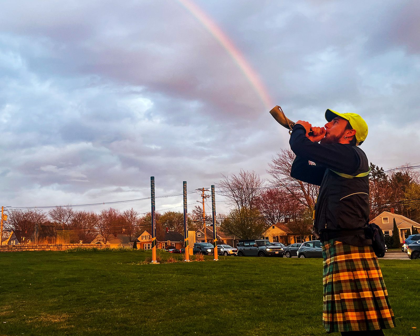 A hasher in a kilt blowing a horn under a rainbow