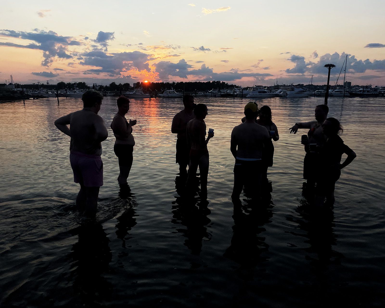 Hashers wading into the water at sunset, in silhouette